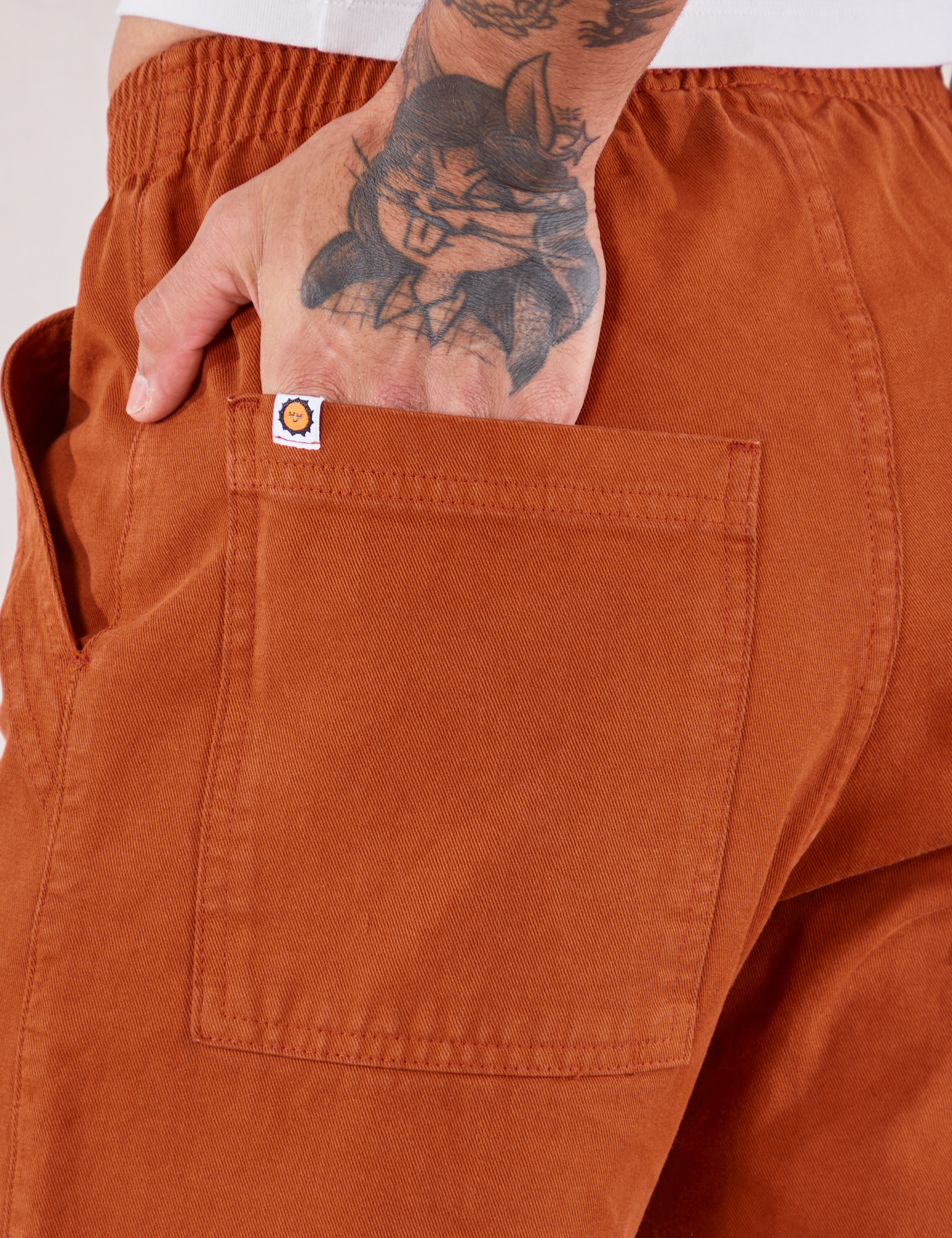 Action Pants in Burnt Terracotta back pocket close up. Jesse has their hand in the pocket.