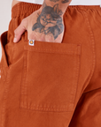 Action Pants in Burnt Terracotta back pocket close up. Jesse has their hand in the pocket.