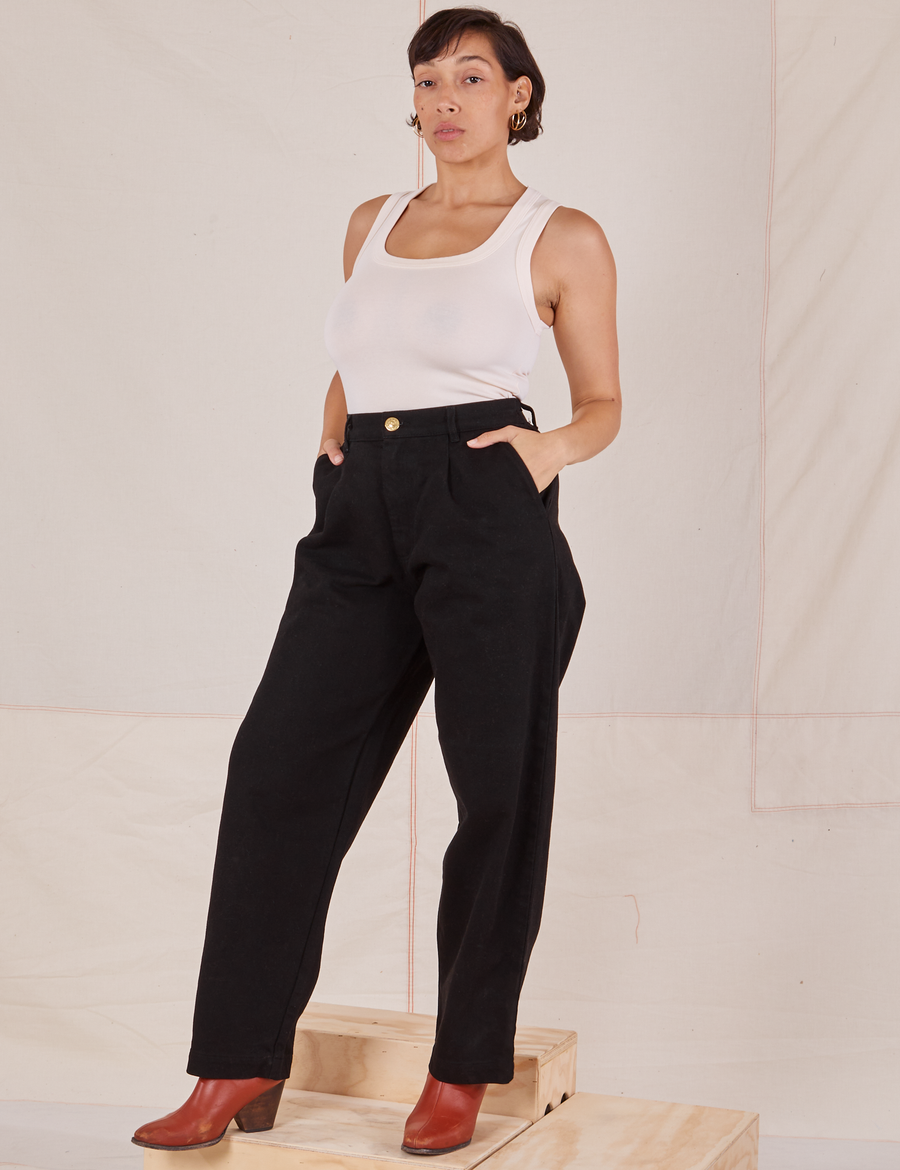 Tiara is wearing Denim Trouser Jeans in Black and a vintage off-white Tank Top. She has both hands in the pockets.