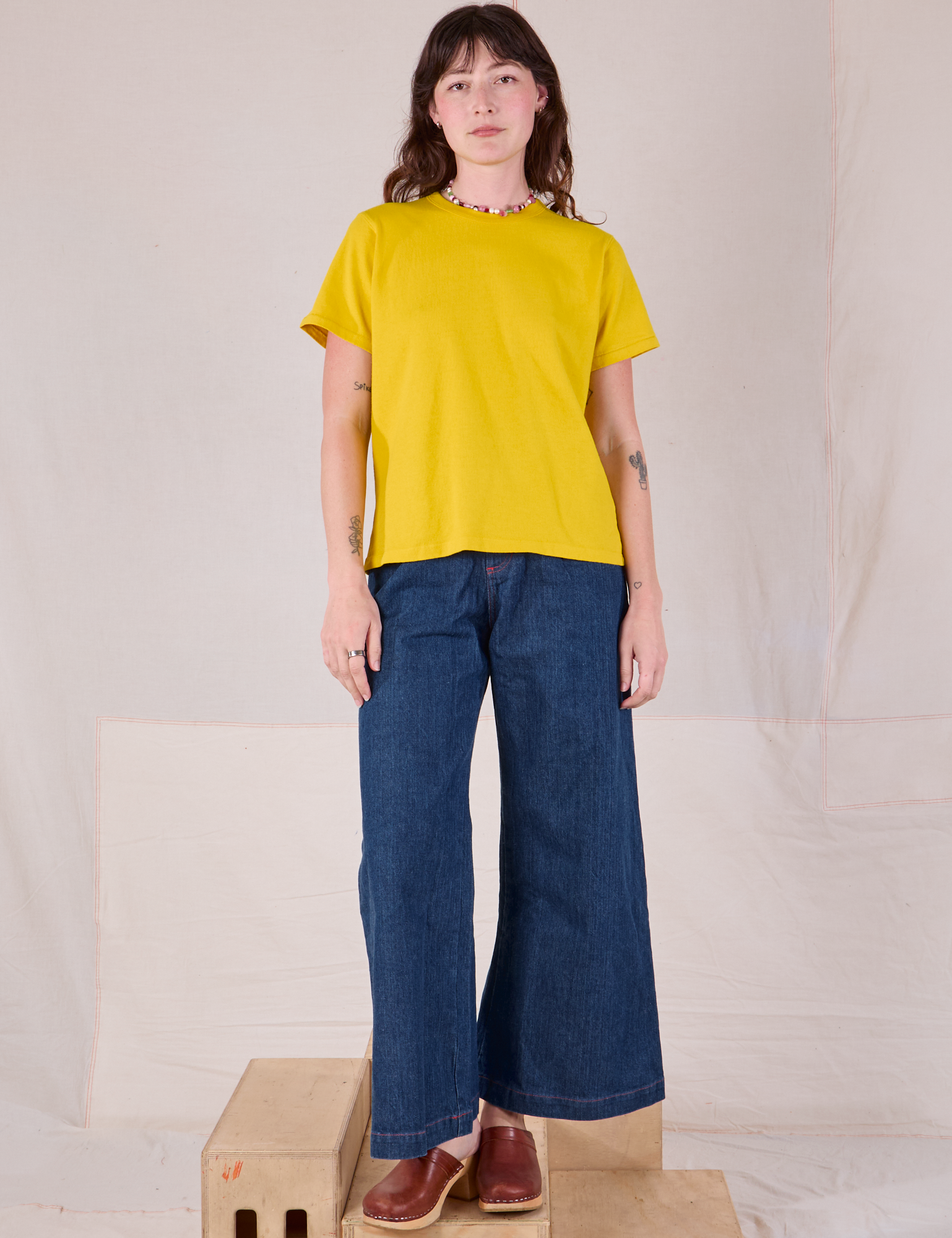 Alex is wearing Burly Tee in Golden Yellow and dark wash Denim Wide Leg Trousers