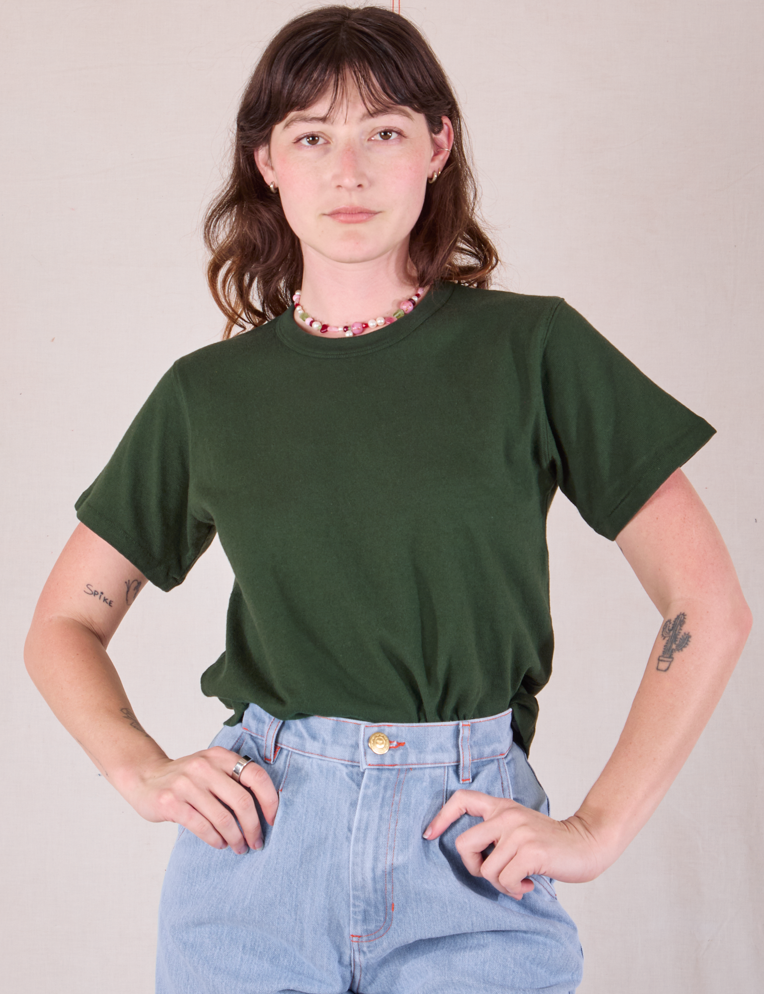 Alex is wearing Burly Tee in Swamp Green tucked into light wash Denim Wide Leg Trousers