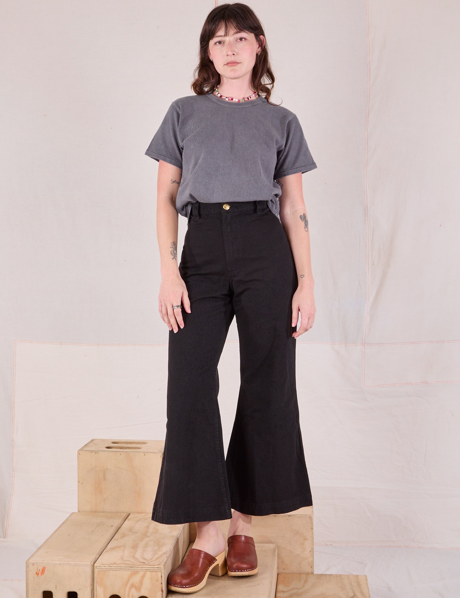 Alex is wearing Burly Tee in Washed Grey tucked into black Bell Bottoms