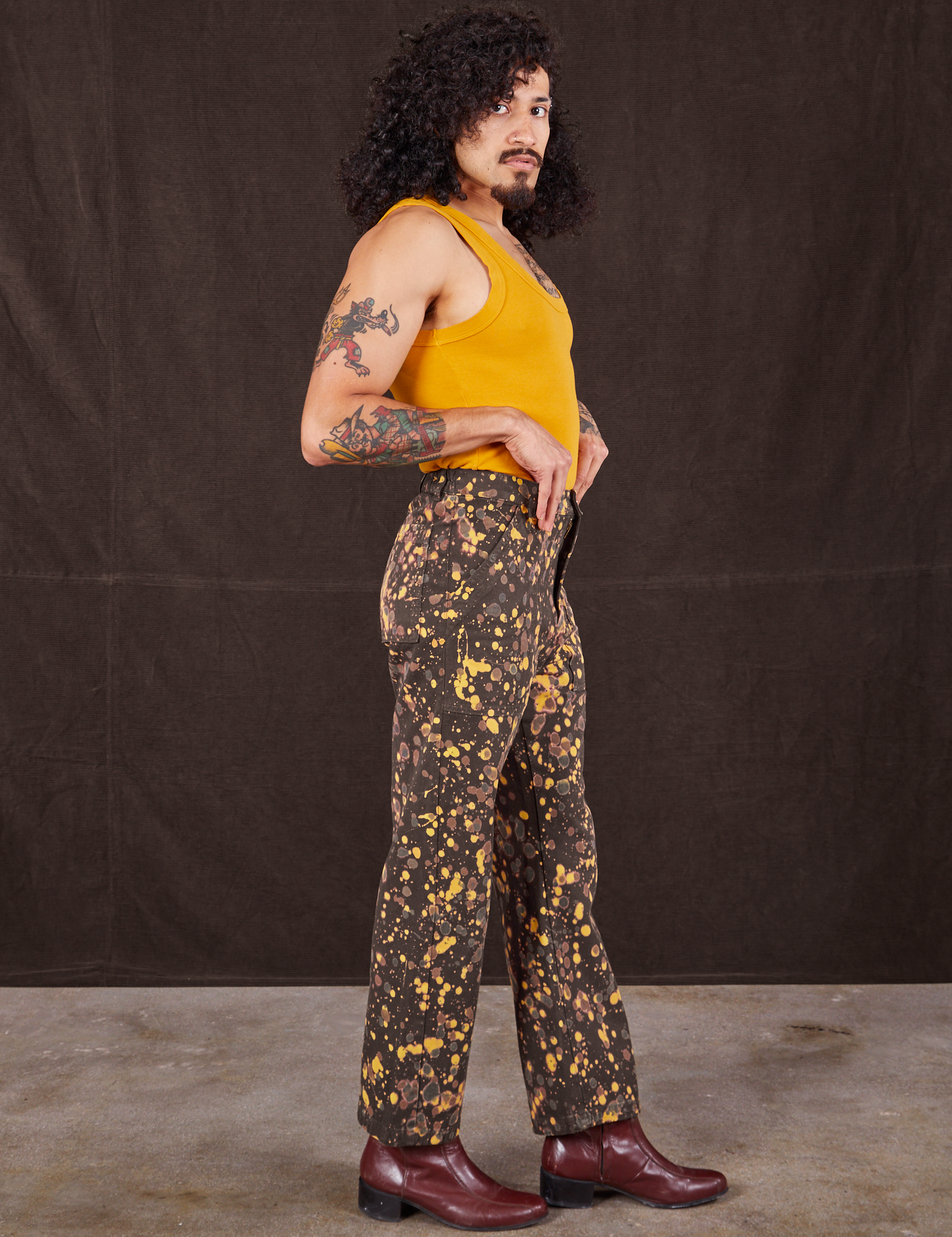 Side view of Marble Splatter Work Pants in Espresso Brown and mustard yellow Tank Top on Jesse