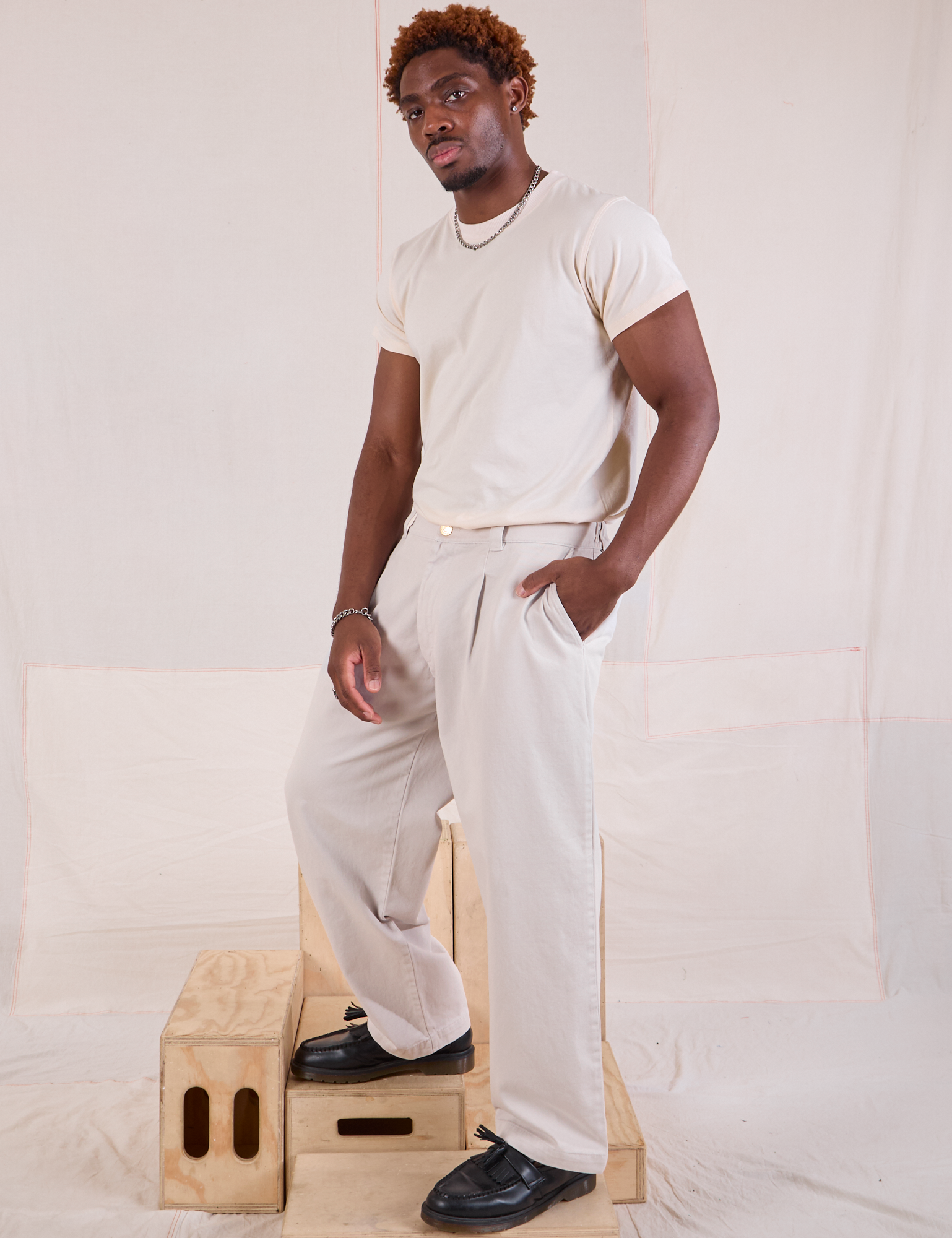 Angled front view of Mid-Rise Pleated Trousers in Stone White and Organic Vintage Tee in vintage tee off-white