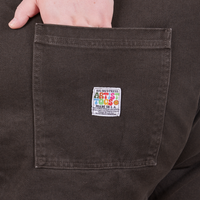 Back pocket close up of Original Overalls in Mono Espresso. Catie has her hand in the pocket.