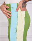 Side close up of Hand-Painted Stripe Western Pants in Bright Olive. Baby blue and off-white hand painted stripe along the side. Jesse has their hand in the back pocket.