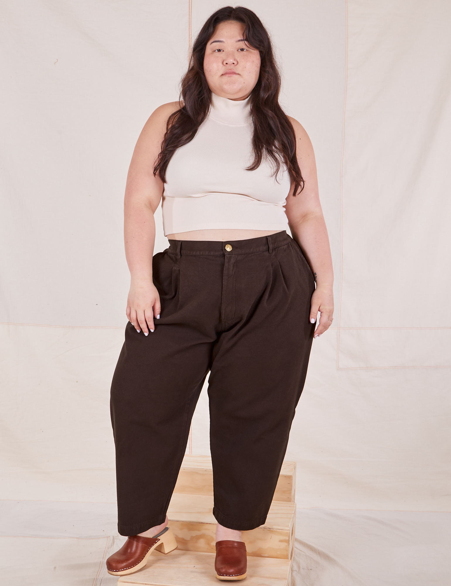 Ashley is 5&#39;7&quot; and wearing 1XL Petite Heritage Trousers in Espresso Brown paired with vintage off-white Sleeveless Turtleneck