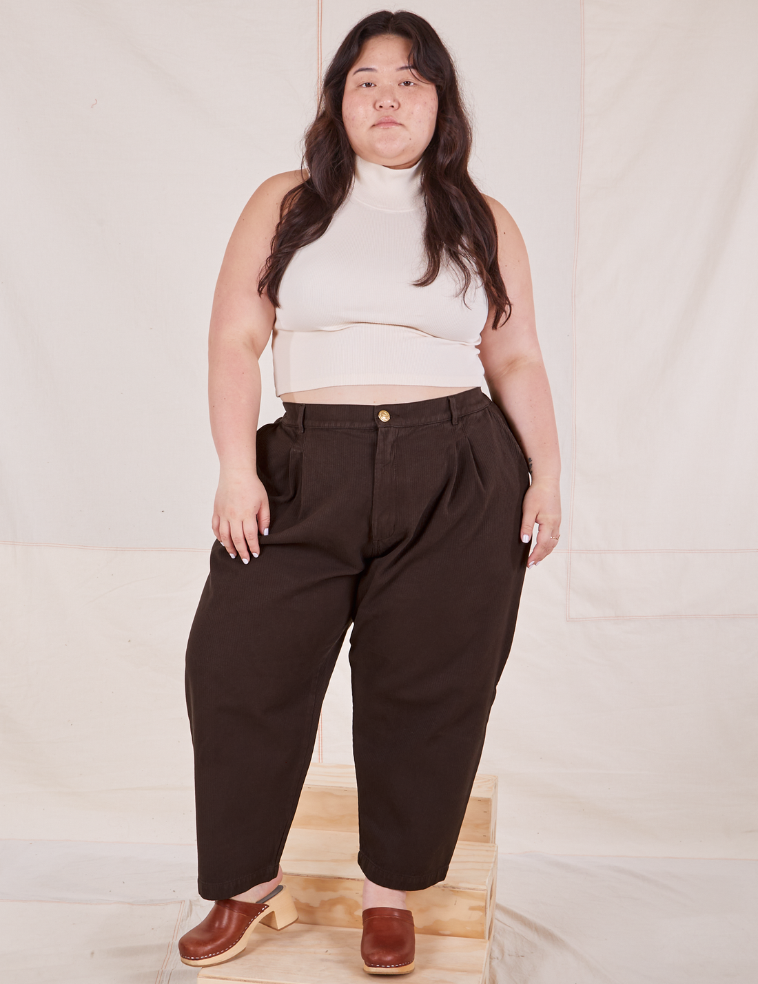 Ashley is 5'7" and wearing 1XL Petite Heritage Trousers in Espresso Brown paired with vintage off-white Sleeveless Turtleneck