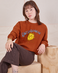 Hana is sitting on a wooden crate wearing Bill Ogden's Sun Baby Crew and espresso brown Western Pants