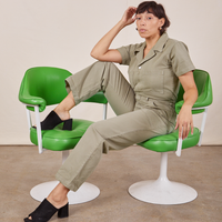 Tiara is sitting in a green chair wearing Short Sleeve Jumpsuit in Khaki Grey