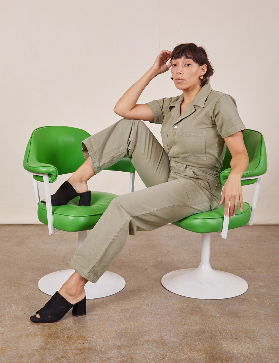 Tiara is sitting in a green chair wearing Short Sleeve Jumpsuit in Khaki Grey
