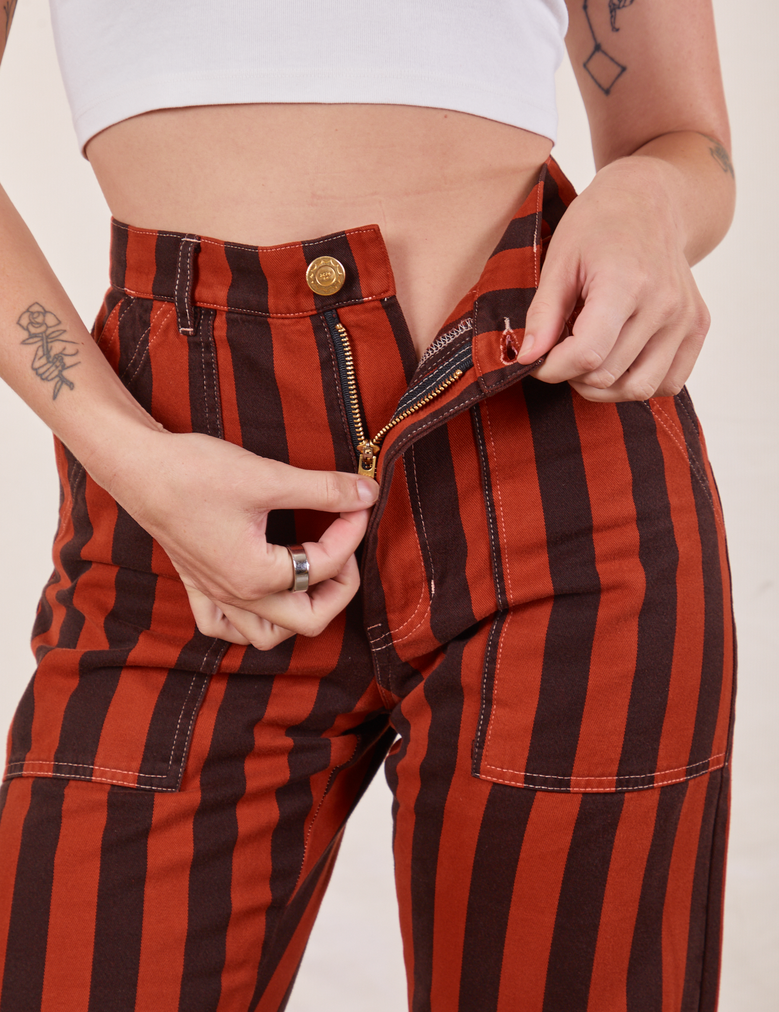 Black Striped Work Pants in Paprika front close up. Alex is pulling on the zipper tab.