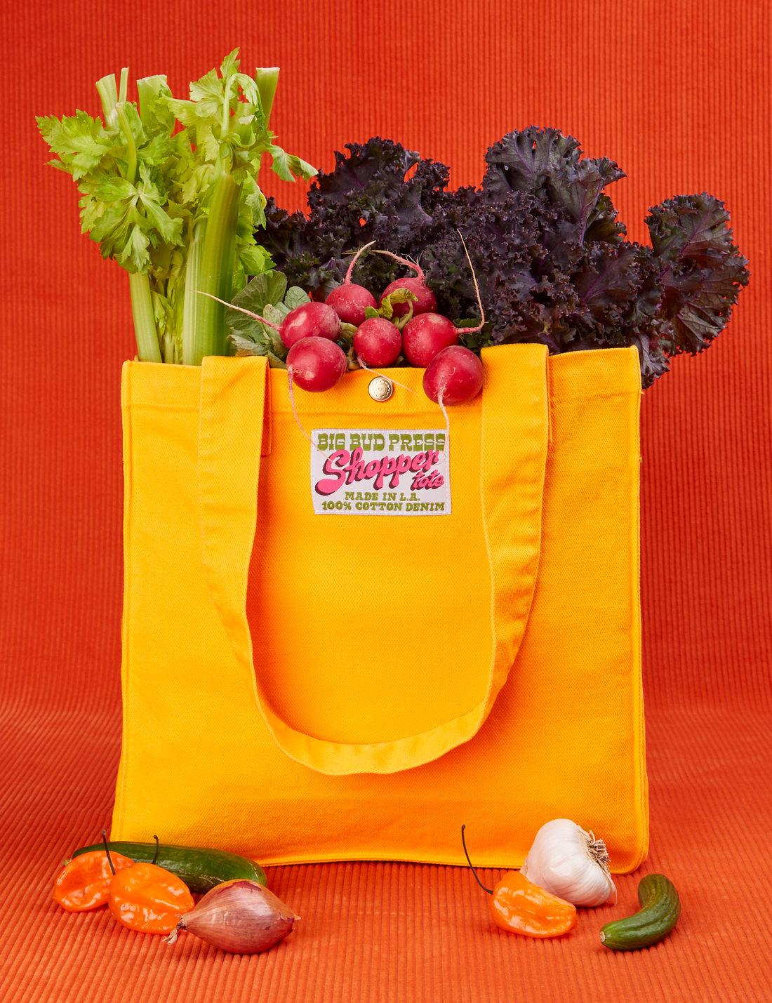 Shopper Tote Bag in Sunshine Yellow with lettuce, celery and radishes in bag. Peppers, cucumber and garlic are place in front of the tote.