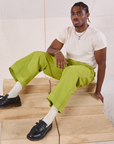 Isaac is wearing Action Pants in Gross Green and sitting on a wooden crate