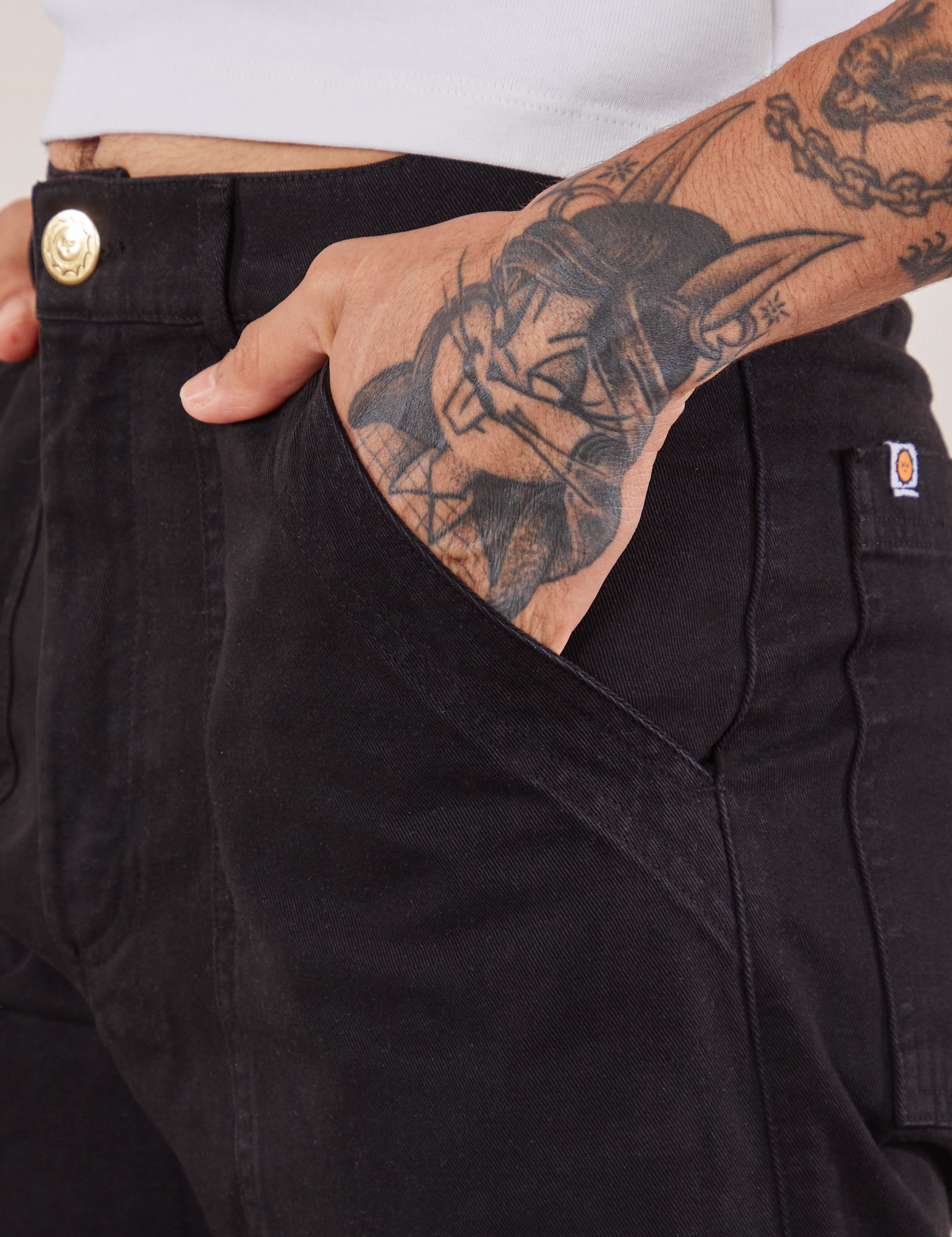 Work Pants in Black front pocket close up. Jesse has their hand in the pocket