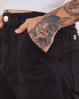 Work Pants in Black front pocket close up. Jesse has their hand in the pocket