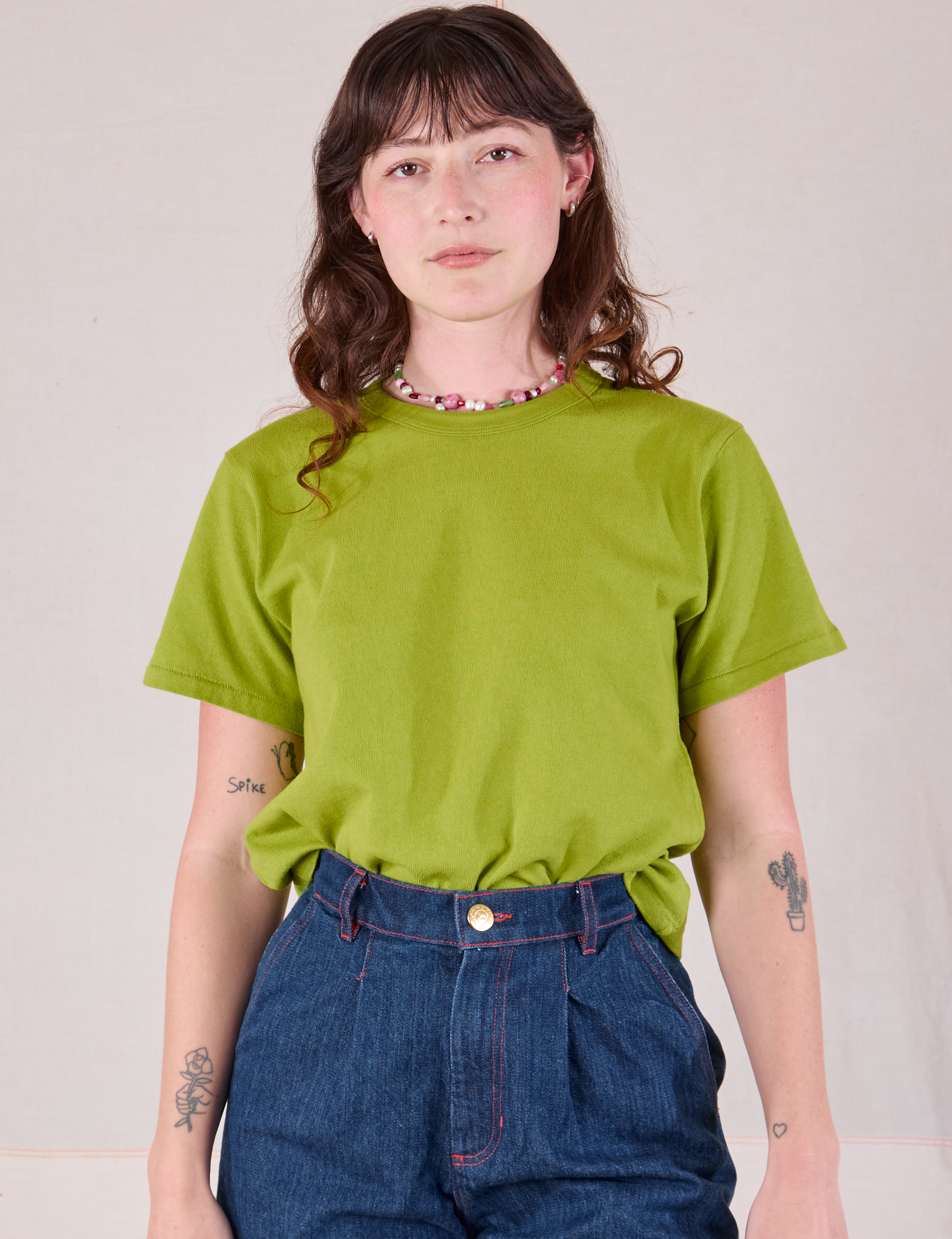 Alex is wearing Burly Tee in Gross Green tucked into her dark wash Denim Wide Leg Trousers