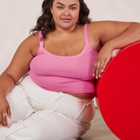 Alicia is sitting on the floor and has her right elbow on a red circular platform. She is wearing Cropped Cami in Bubblegum Pink and vintage off-white Western Pants.