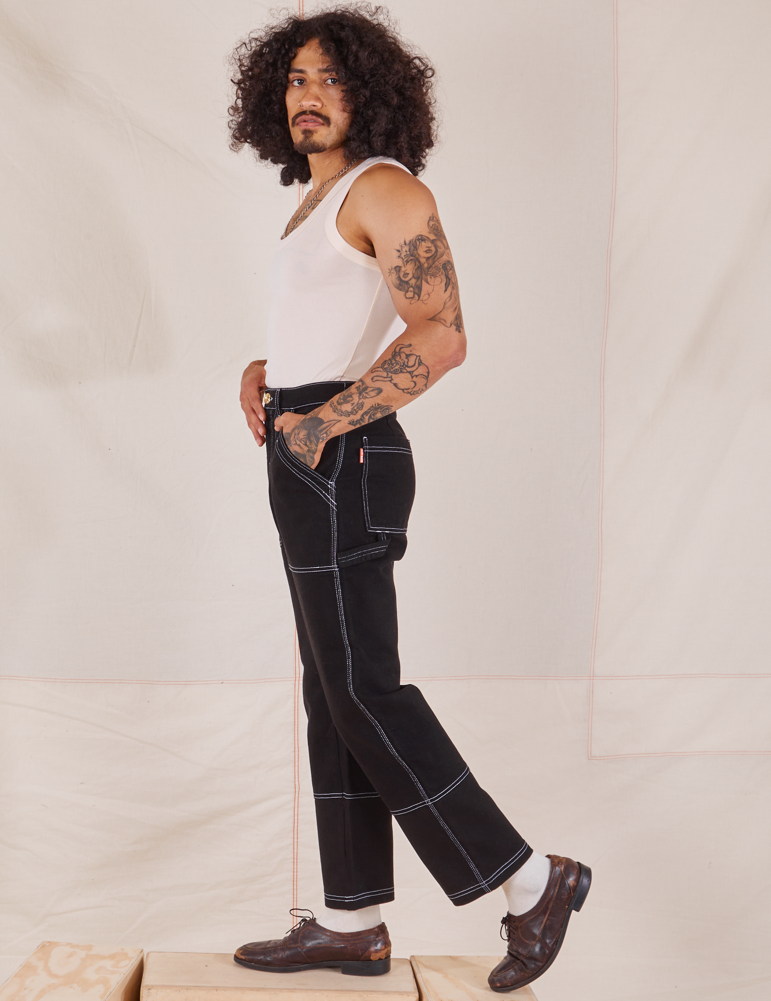 Side view of Carpenter Jeans in Black and vintage off-white Tank Top worn by Jesse