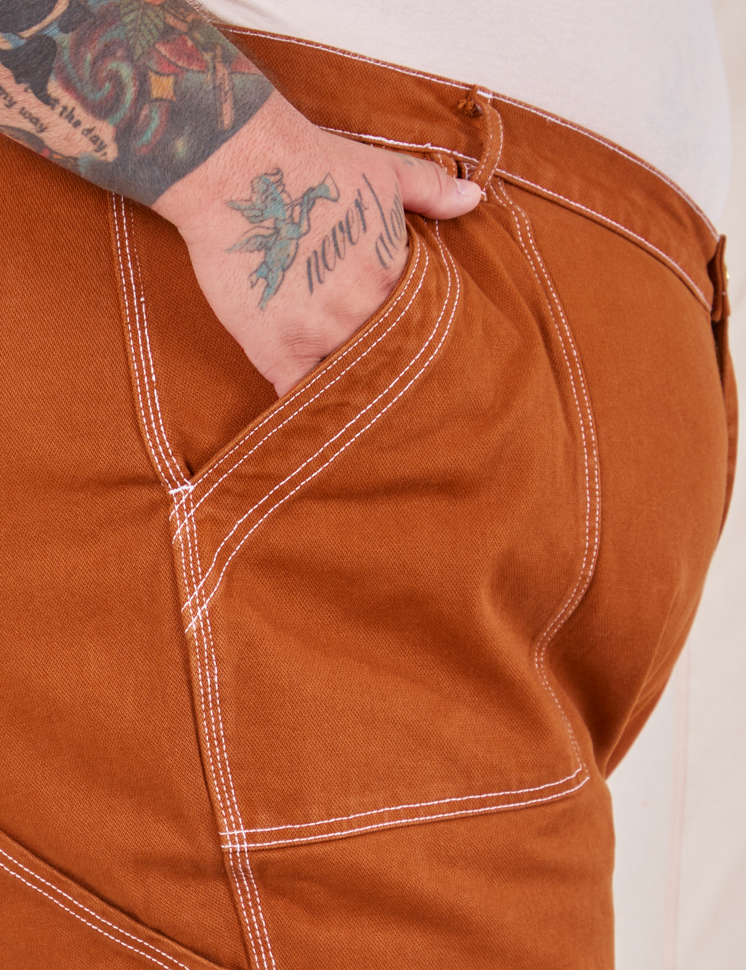 Carpenter Jeans in Burnt Terracotta front pocket close up. Sam has their hand in the pocket.
