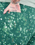 Back pocket close up of Marble Splatter Work Pants in Hunter Green. Sam has their hand in the pocket.