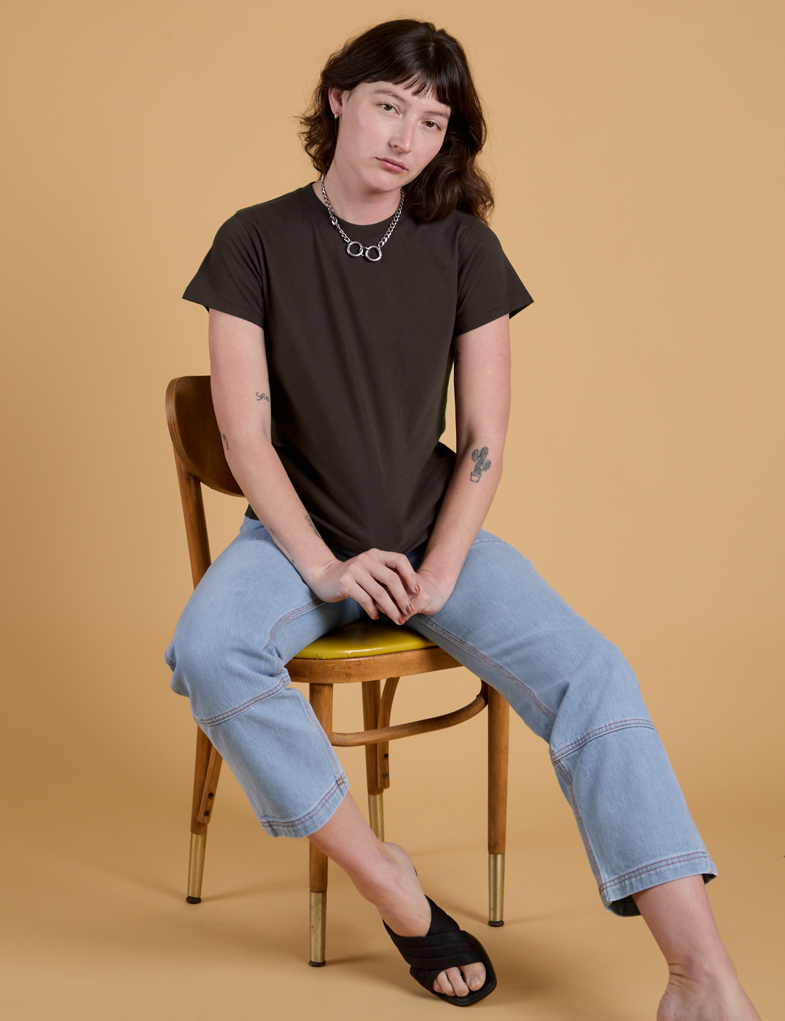 Alex is wearing Organic Vintage Tee in Espresso Brown and light wash Carpenter Jeans and sitting in a chair