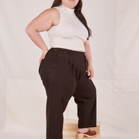 Angled view of Heritage Trousers in Espresso Brown and vintage off-white Sleeveless Essential Turtleneck worn by Ashley