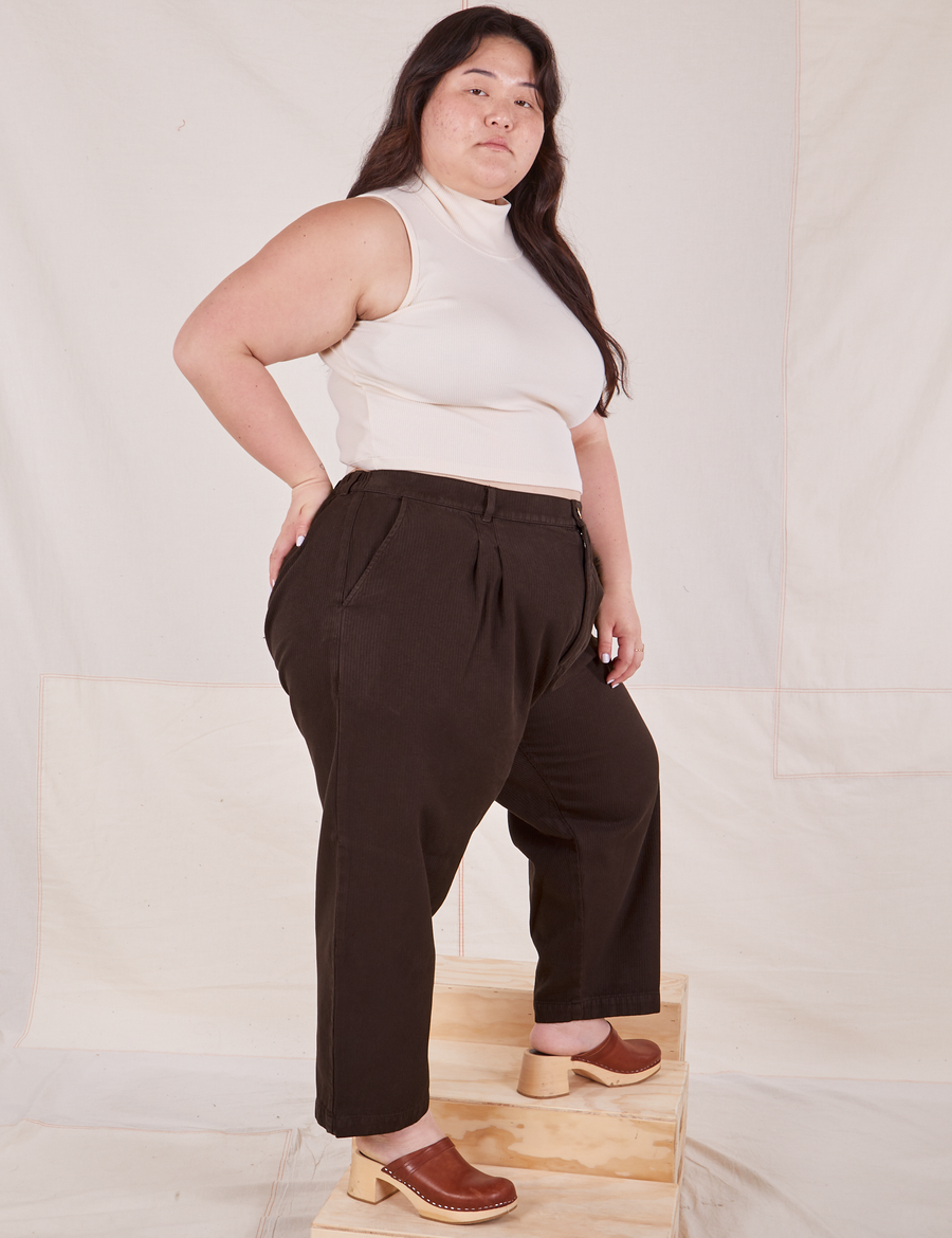Angled view of Heritage Trousers in Espresso Brown and vintage off-white Sleeveless Essential Turtleneck worn by Ashley