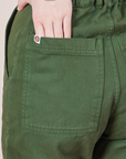 Back pocket close up of Petite Short Sleeve Jumpsuit in Dark Emerald Green. Hana has her hand in the back pocket.