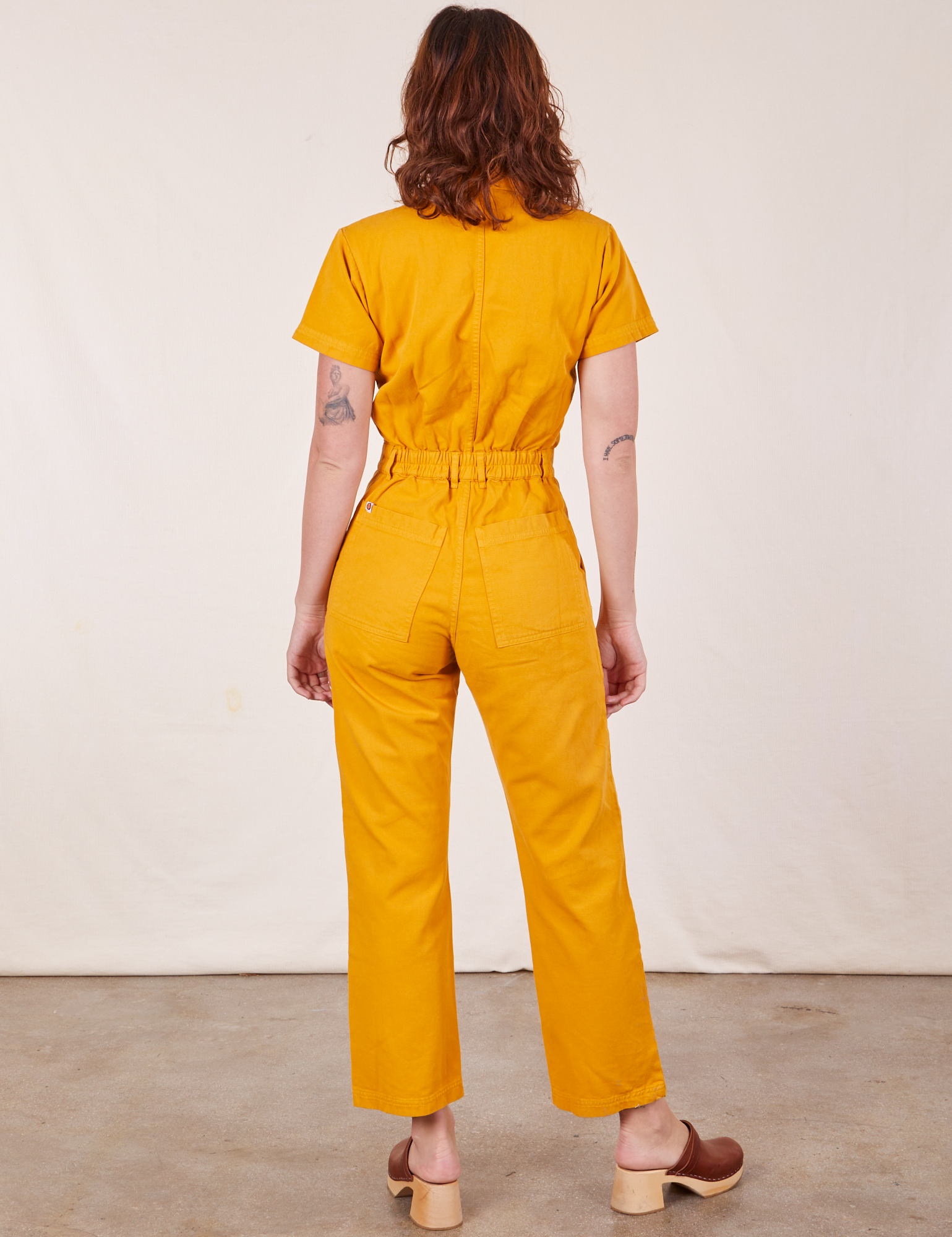 Back view of Short Sleeve Jumpsuit in Mustard Yellow worn by Alex