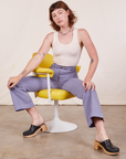 Alex is sitting in a yellow and white chair wearing Western Pants in Faded Grape and a vintage off-white Tank Top