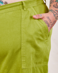 Work Pants in Gross Green front pocket close up. Sam has their hand in the pocket.