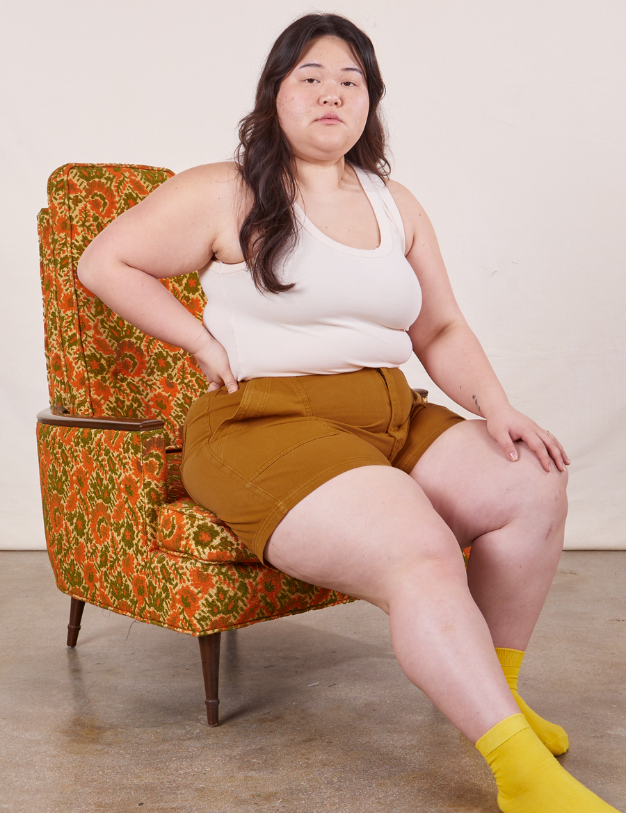 Ashley is sitting in an vintage floral upholstered chair wearing Classic Work Shorts in Spicy Mustard paired with vintage off-white Tank Top