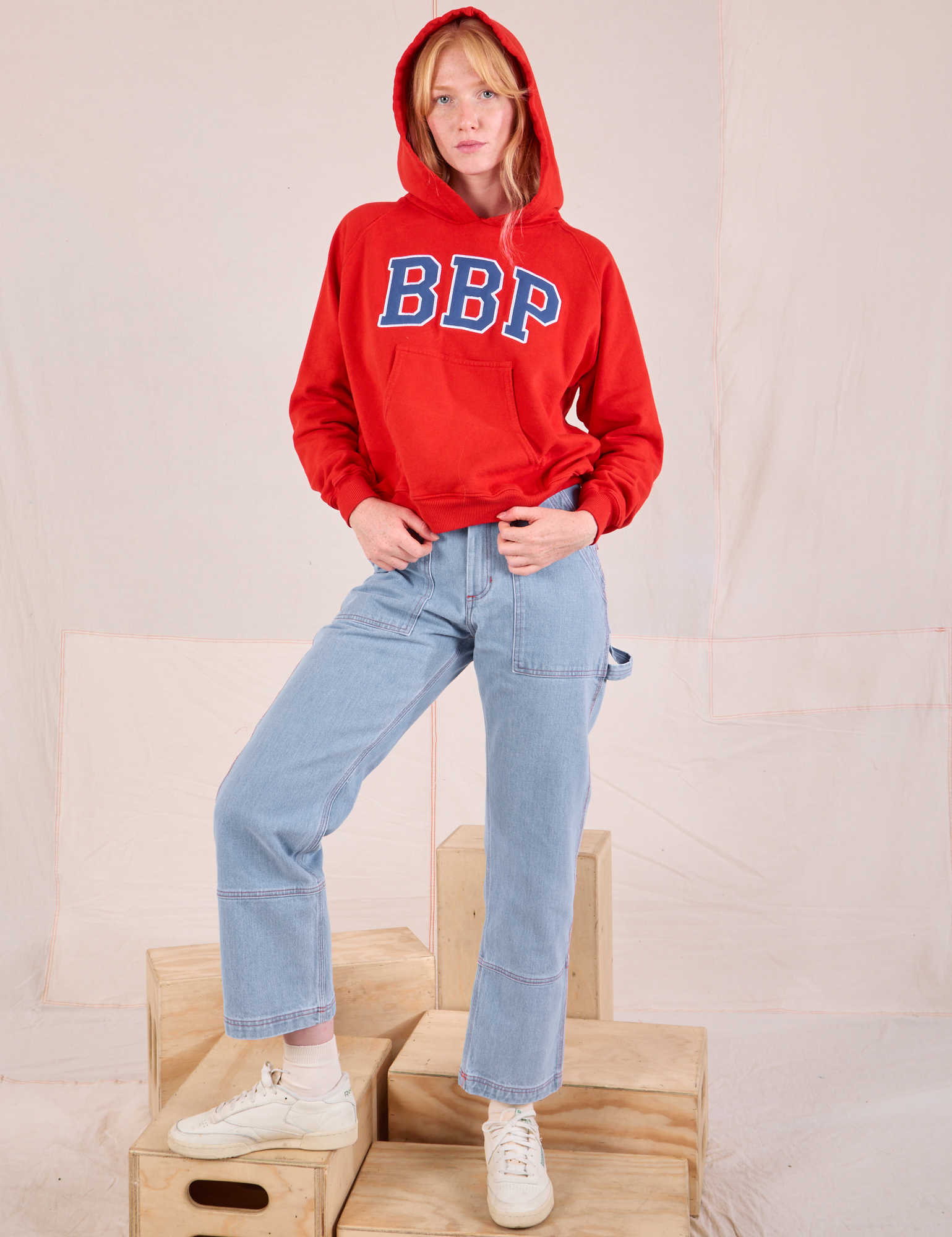 Margaret is wearing Collegiate Hoodie in Mustang Red paired with light wash Carpenter Jeans