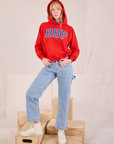 Margaret is wearing Collegiate Hoodie in Mustang Red paired with light wash Carpenter Jeans