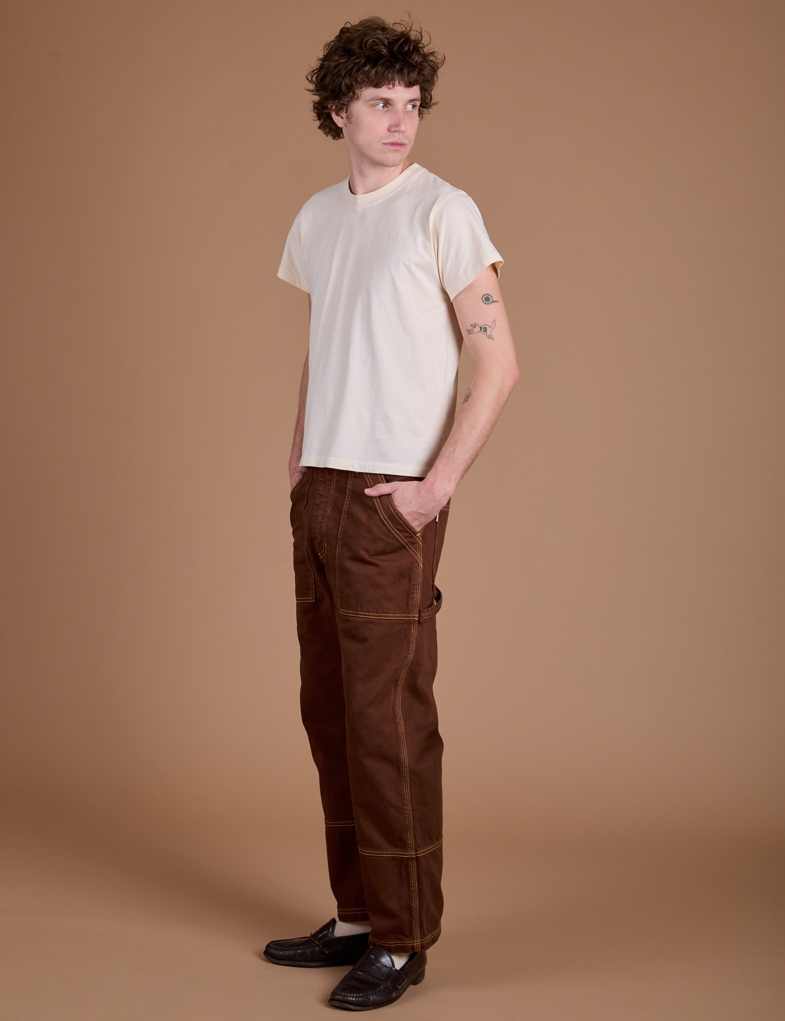 Angled front view of Carpenter Jeans in Fudgesicle Brown and Organic Tee in Vintage Tee Off-White