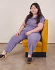 Ashley is sitting in a mustard yellow vinyl booth seat wearing Petite Short Sleeve Jumpsuit in Faded Grape