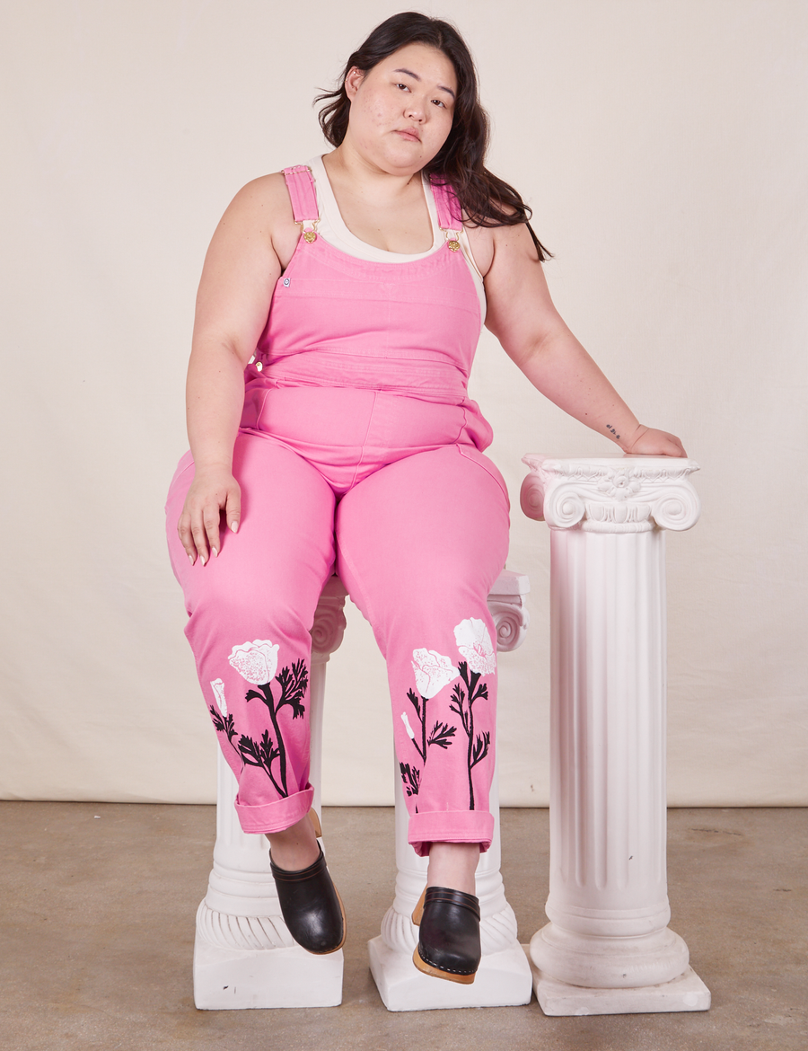 Ashley is sitting on white columns wearing California Poppy Overalls in Bubblegum Pink and vintage off-white Tank Top