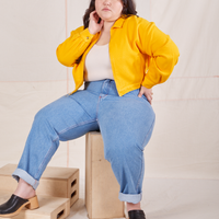 Ashley is sitting on a wooden crate wearing the Ricky Jacket in Sunshine Yellow, a vintage off-white Tank Top and light wash Frontier Jeans