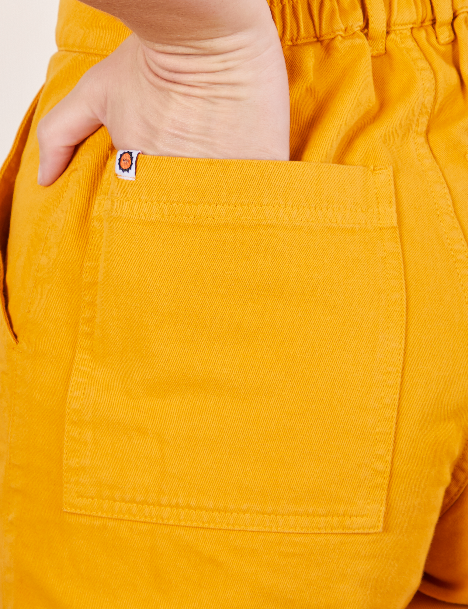Back pocket close up of Short Sleeve Jumpsuit in Mustard Yellow. Alex has her hand in the pocket.