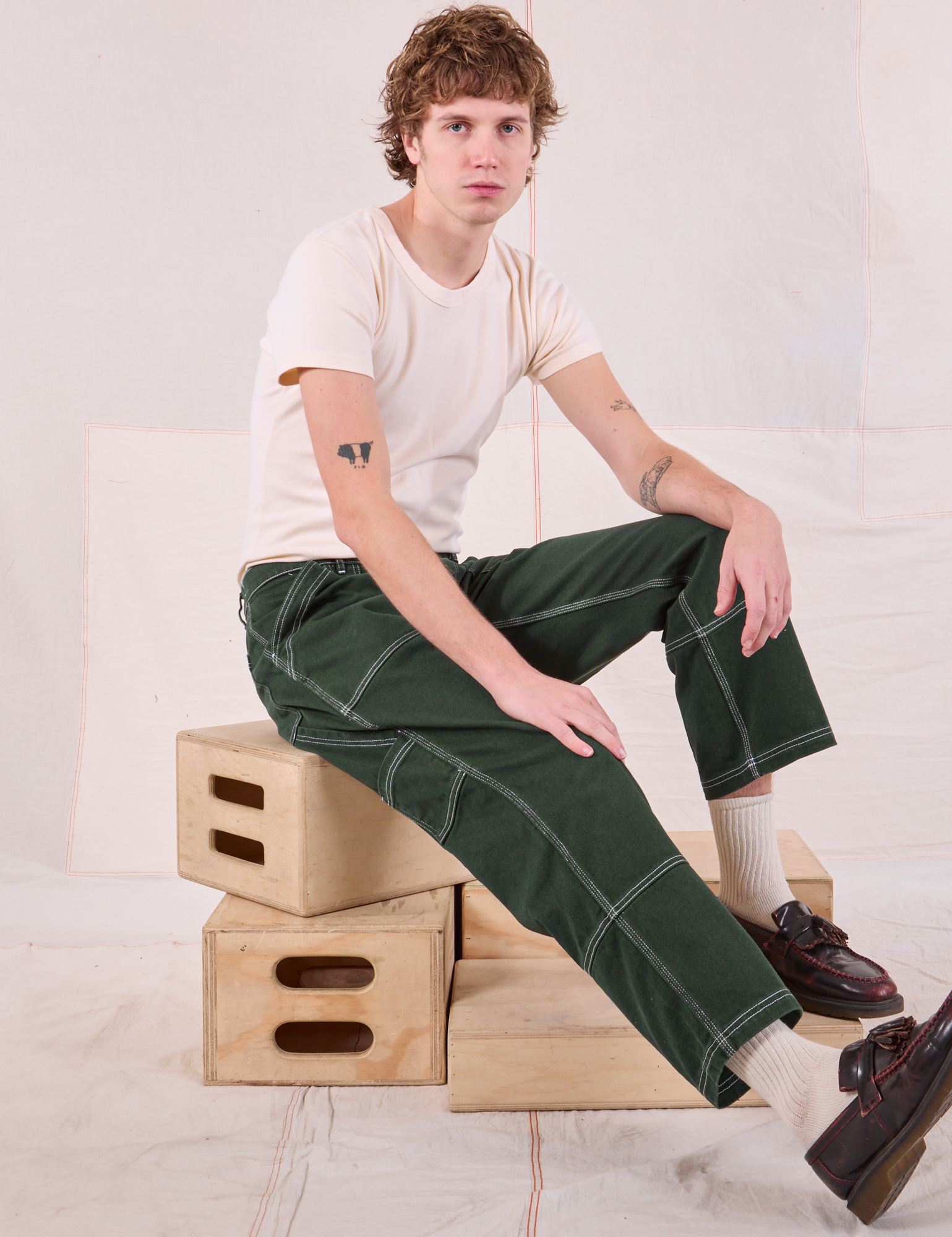 Quinn is sitting in his Carpenter Jeans in Swamp Green