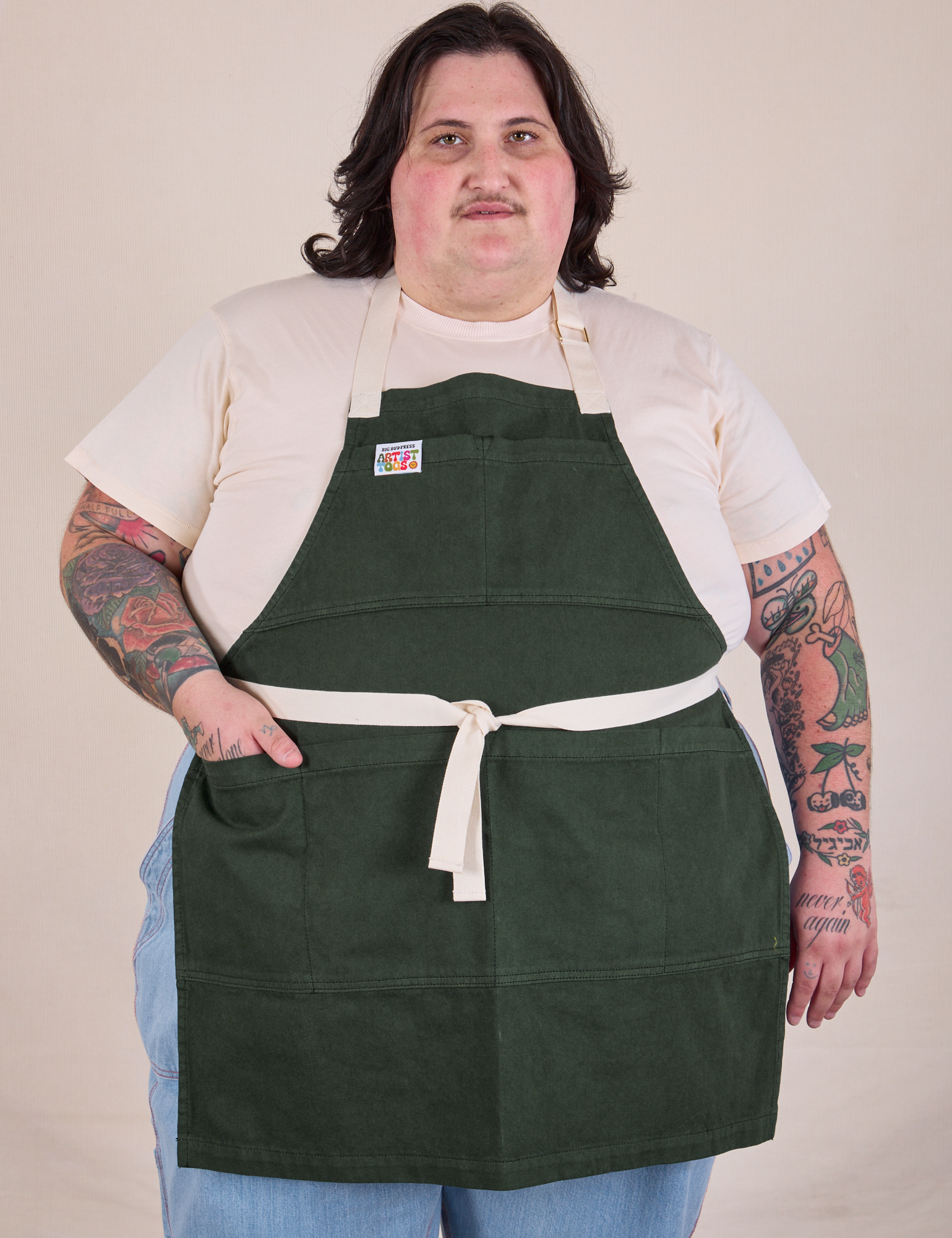 Sam is wearing Full Denim Apron in Swamp Green