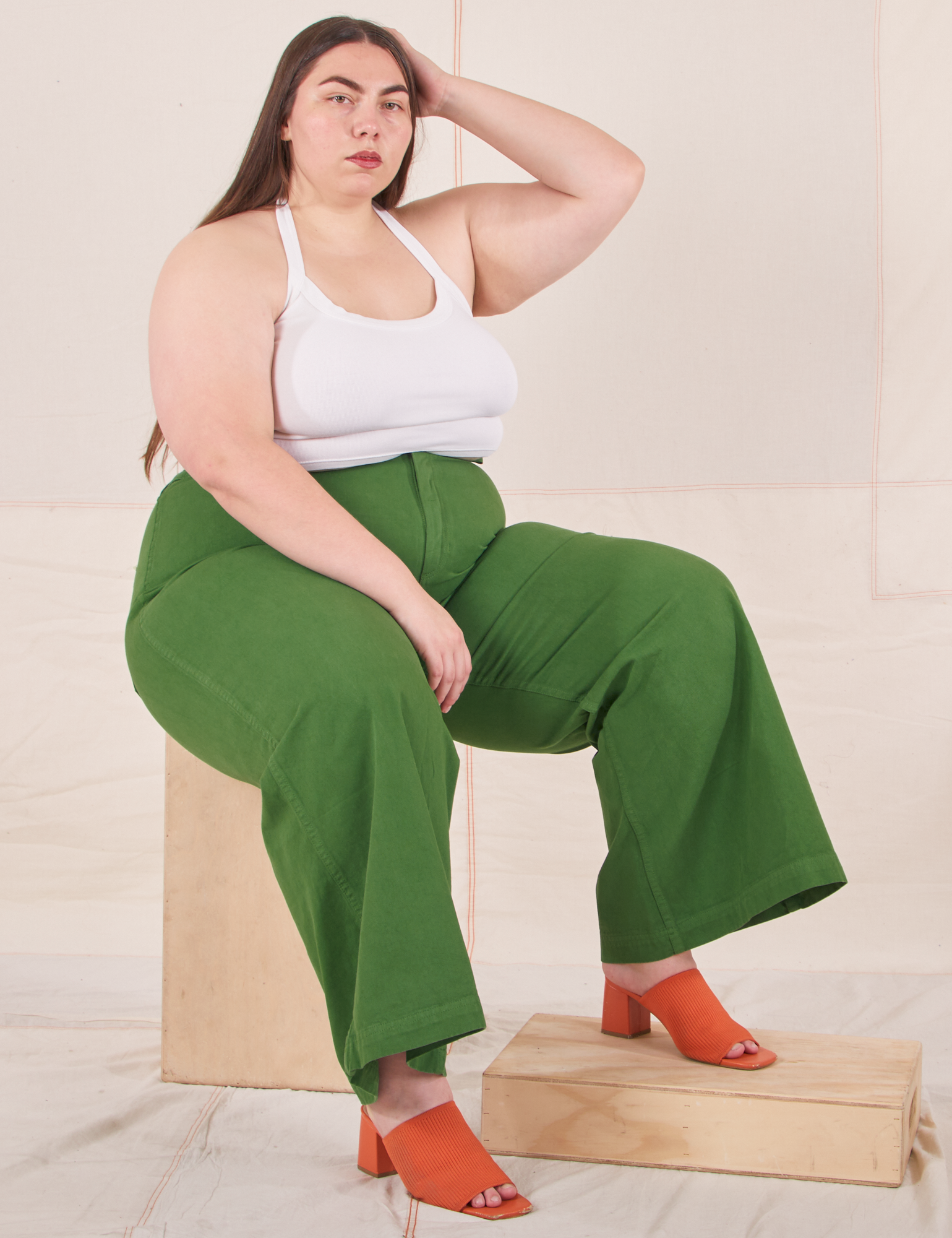 Marielena is sitting on a wooden crate wearing Bell Bottoms in Lawn Green and vintage off-white Halter Top
