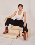 Tiara is sitting on a wooden crate wearing Denim Trouser Jeans in Black and a vintage off-white Tank Top