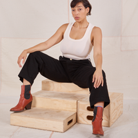 Tiara is sitting on a wooden crate wearing Denim Trouser Jeans in Black and a vintage off-white Tank Top