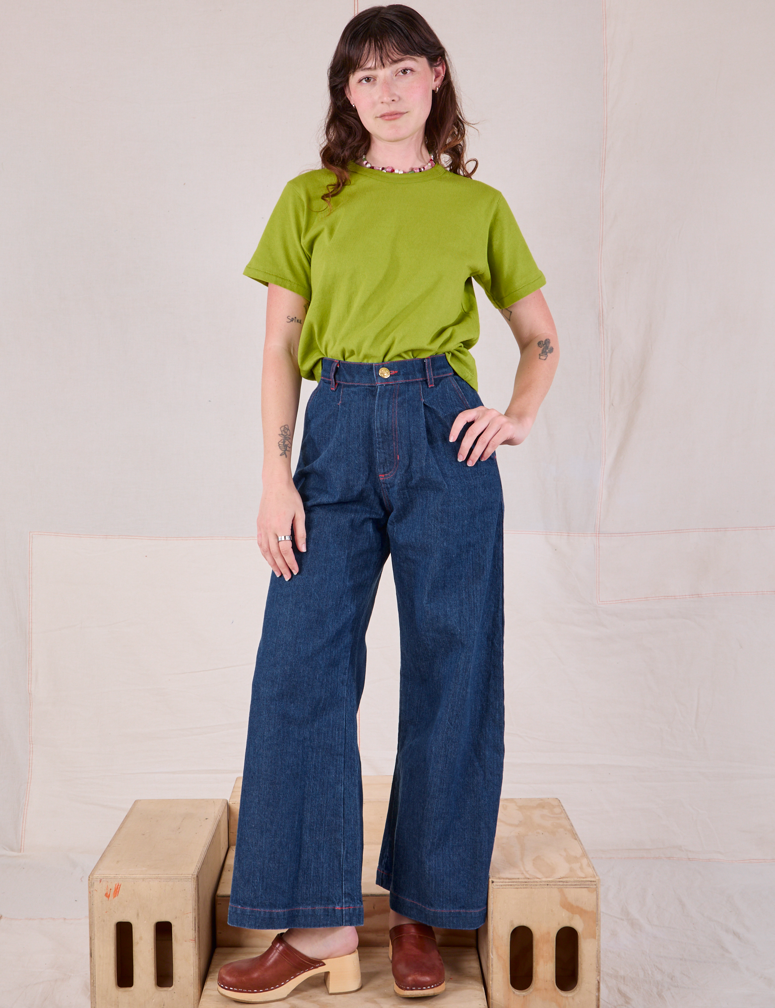 Alex is wearing Burly Tee in Gross Green and dark wash Denim Wide Leg Trousers