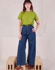 Alex is wearing Burly Tee in Gross Green and dark wash Denim Wide Leg Trousers