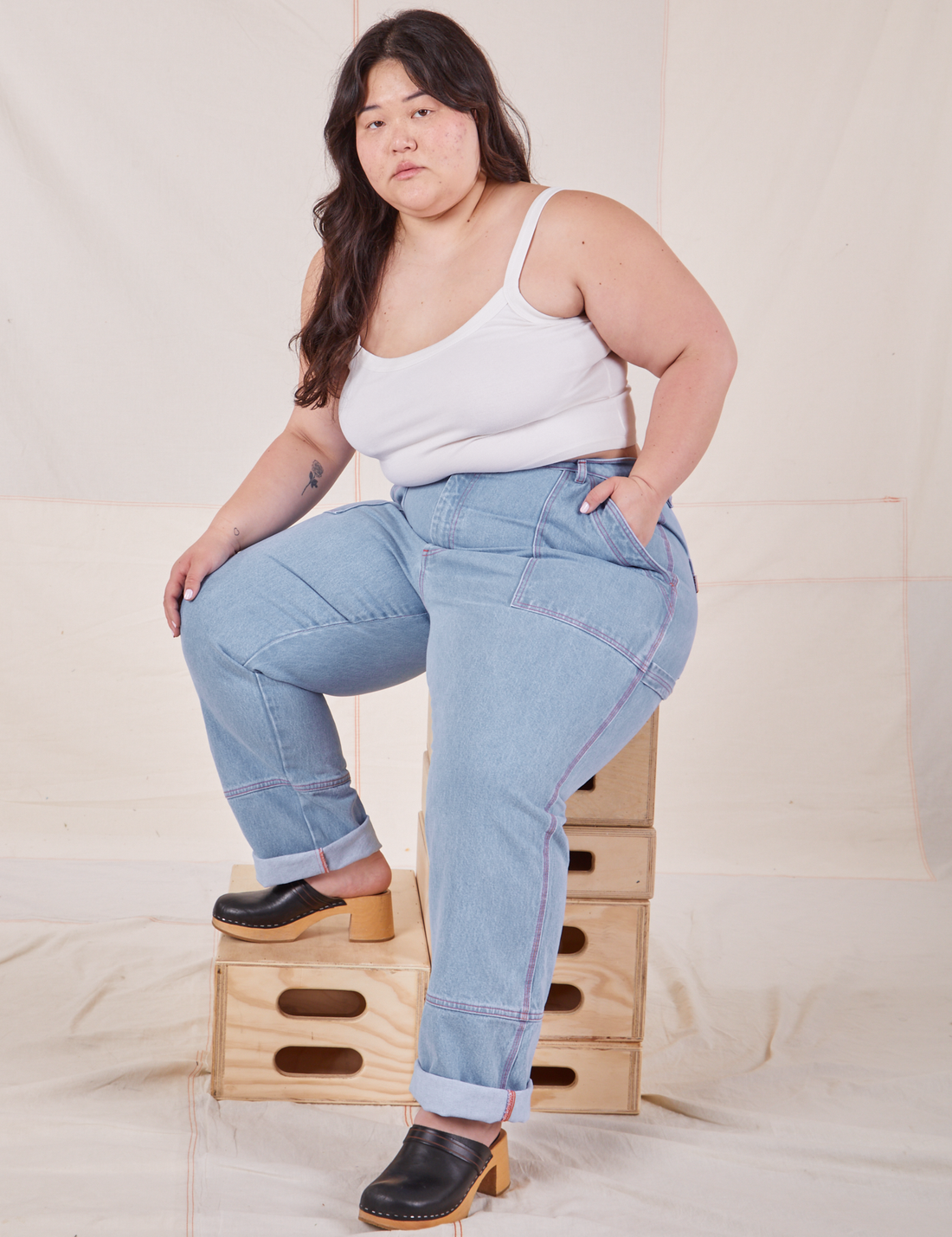 Ashley is sitting on a stack of wooden crates wearing Carpenter Jeans in Light Wash