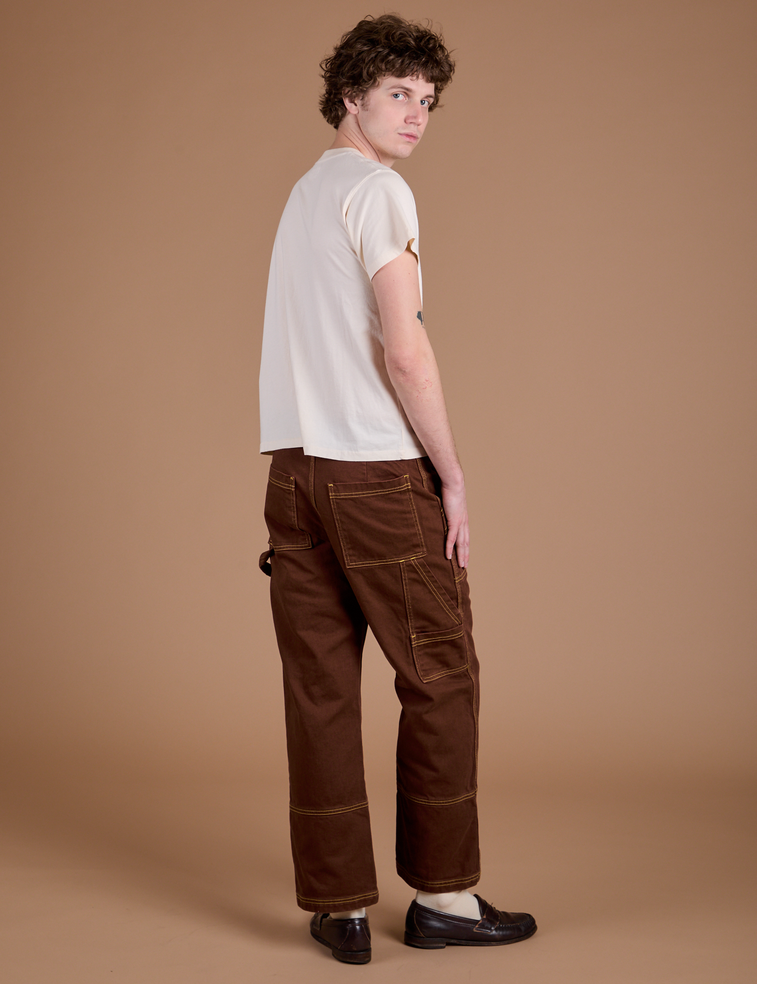 Angled back view of Carpenter Jeans in Fudgesicle Brown and Organic Vintage Tee in Vintage Tee Off-White on Quinn