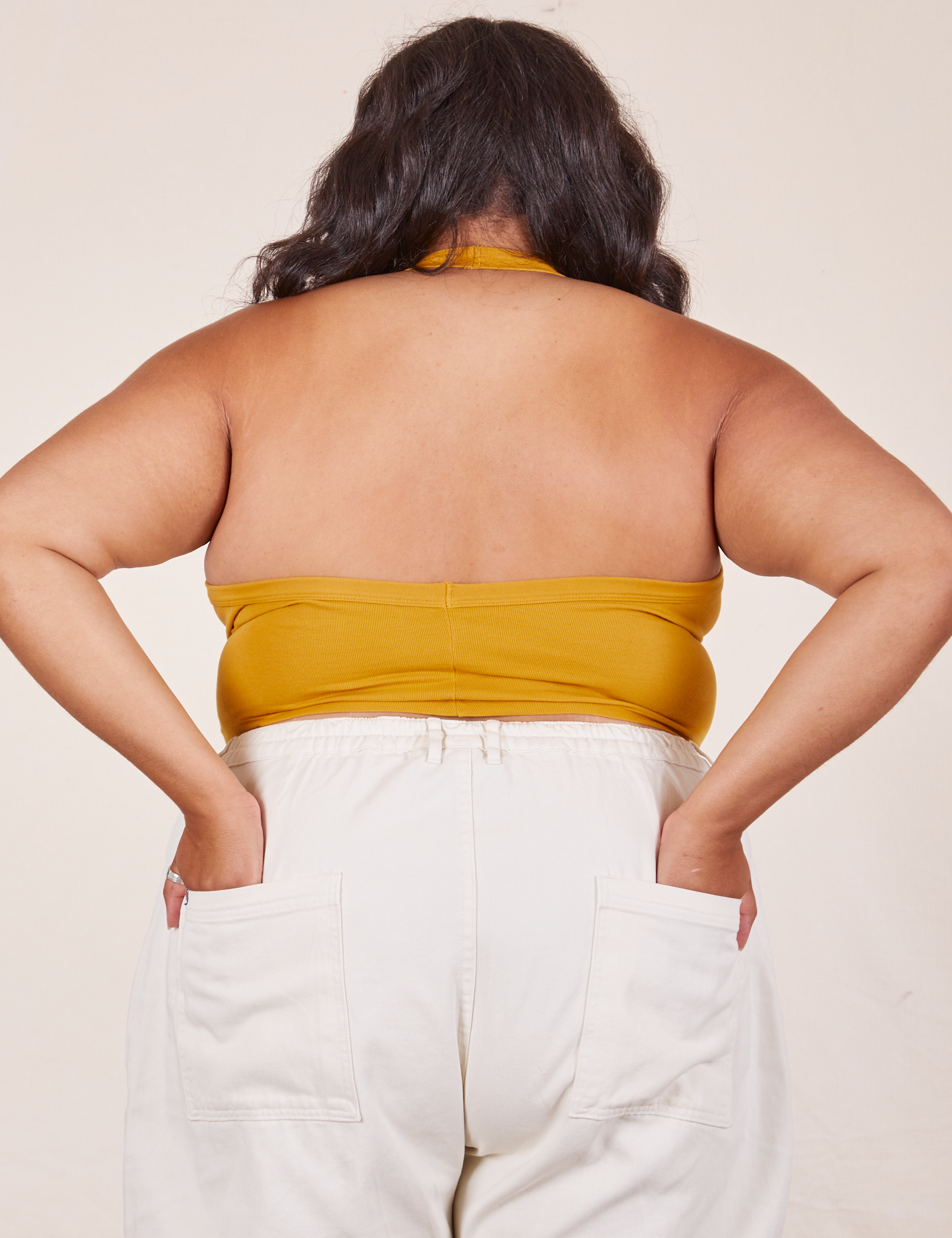 Back view of Halter Top in Mustard Yellow and vintage off-white Western Pants worn by Alicia. She has both of her hands in the back pant pockets.